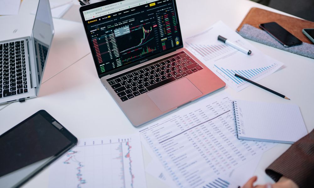 Laptops on a desk displaying stock market charts and financial documents.