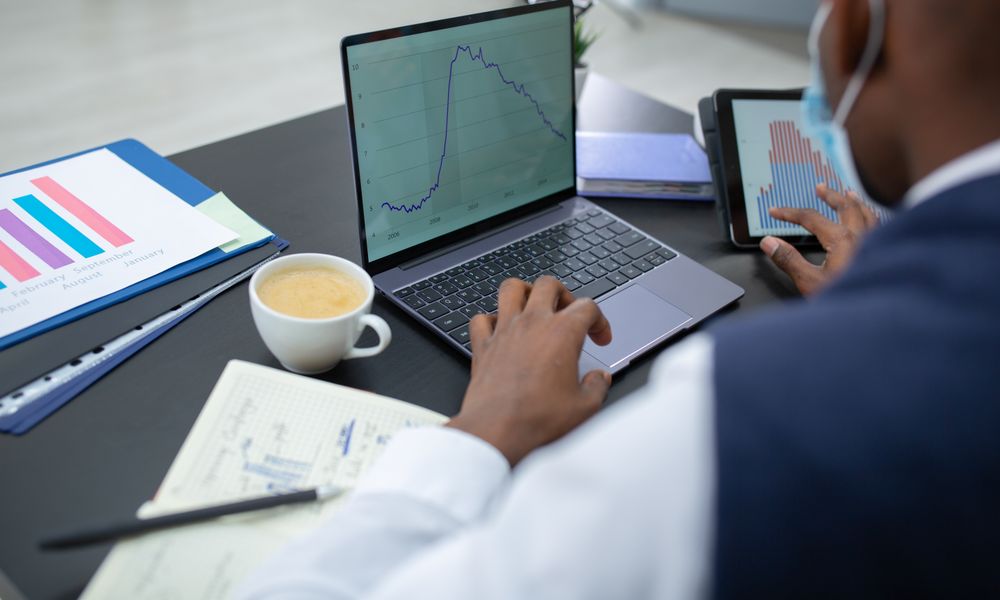 Focused professional analyzing data with laptop and tablet in modern office setting.
