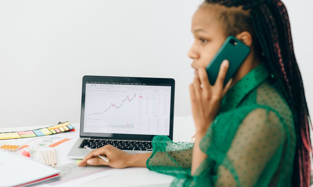 African American woman reviewing stock market charts on a laptop while talking on the phone.
