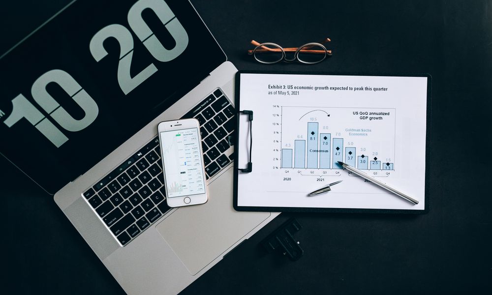 Top view of financial analysis tools on a desk including a laptop, smartphone, and graphs.