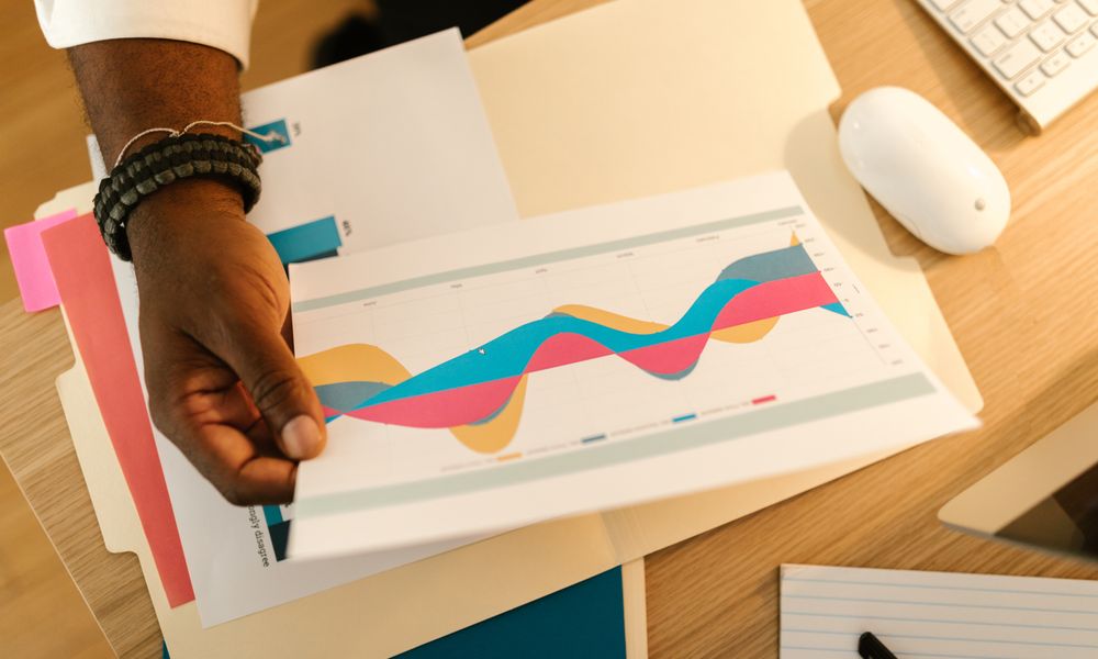 A person's hand holds a printed business graph paper on a desk with office supplies.