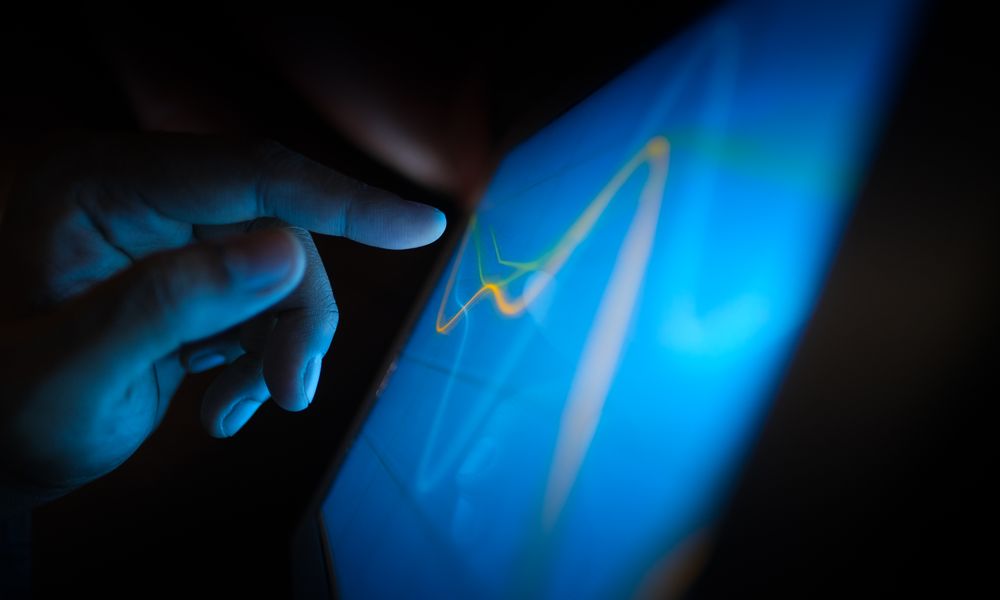 Close-up of a hand interacting with a touchscreen displaying dynamic graphs.