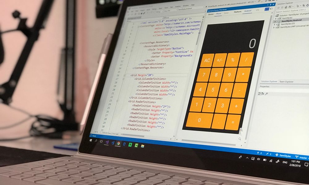 A laptop screen shows a coding application with a calculator design in a tech office setting.