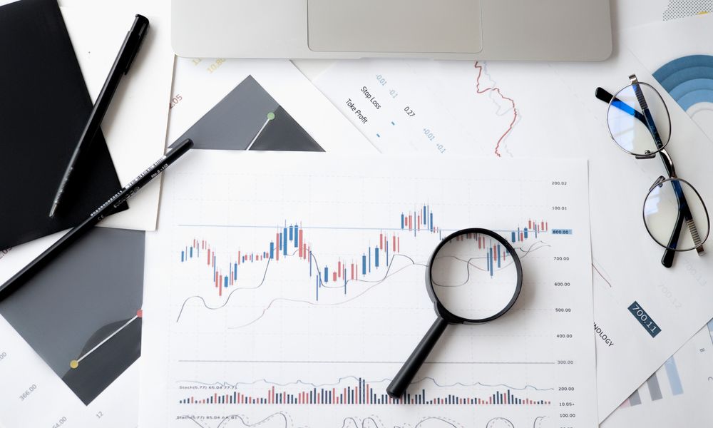 Flat lay of stock market analysis documents with magnifying glass, pens, and glasses.