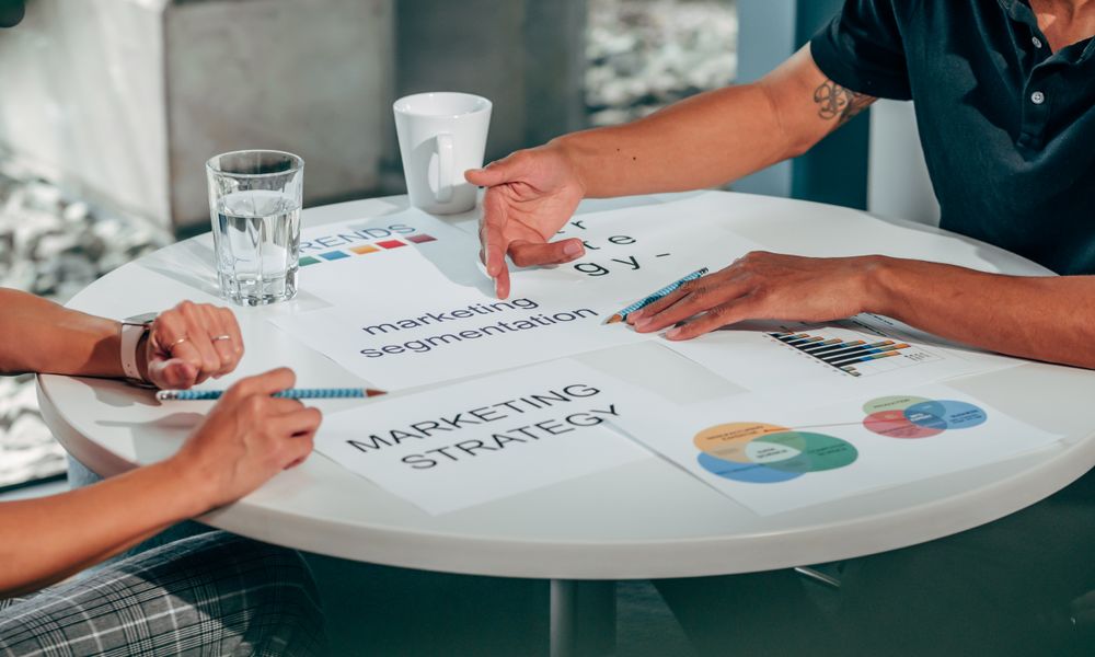 Two adults in an office discussing marketing strategy around a round table.