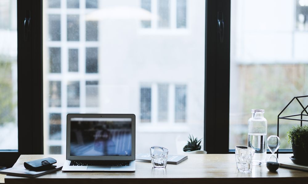 Sleek office desk setup featuring a laptop, glass of water, and open window view.