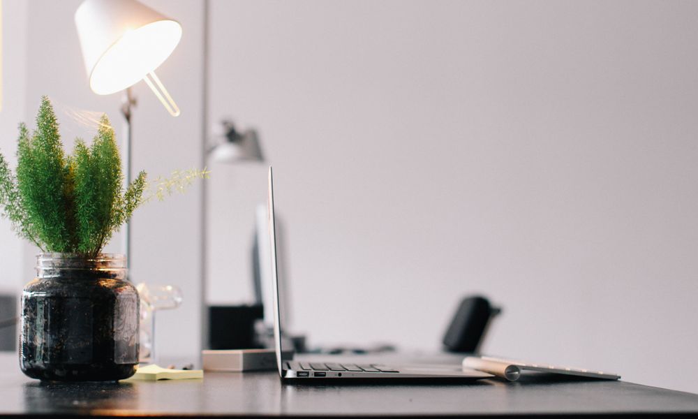 Stylish modern office desk with laptop, lamp, and indoor plant for productive work environment.