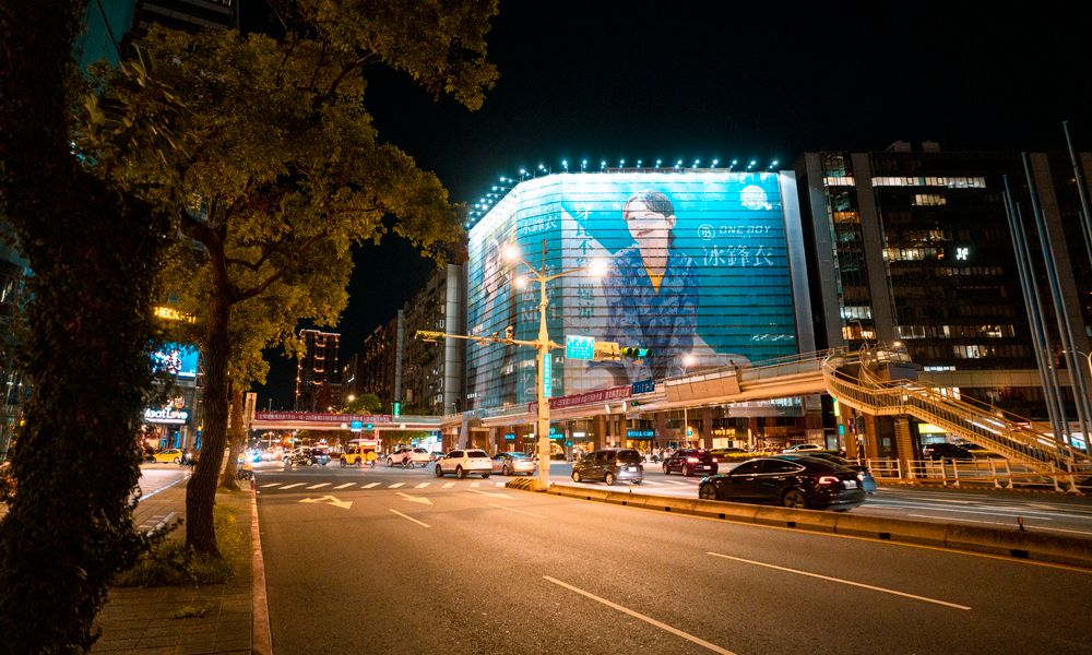 Bustling urban night scene featuring lighted billboards, cars, and city streets.