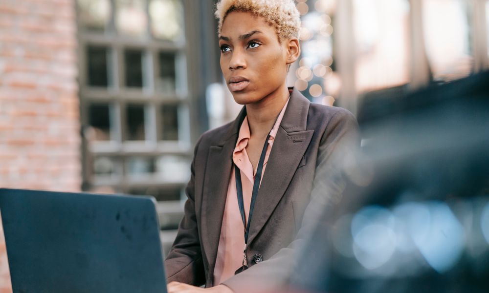 Concentrated African American businesswoman typing on netbook during remote work and thoughtfully looking away