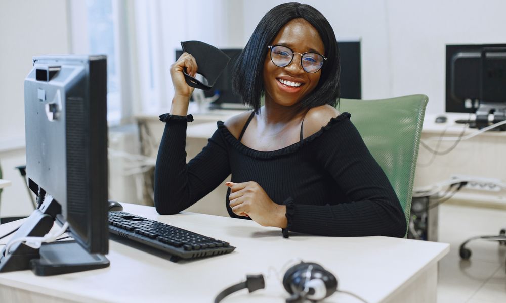 Smiling African American woman at office desk wearing glasses and black top.