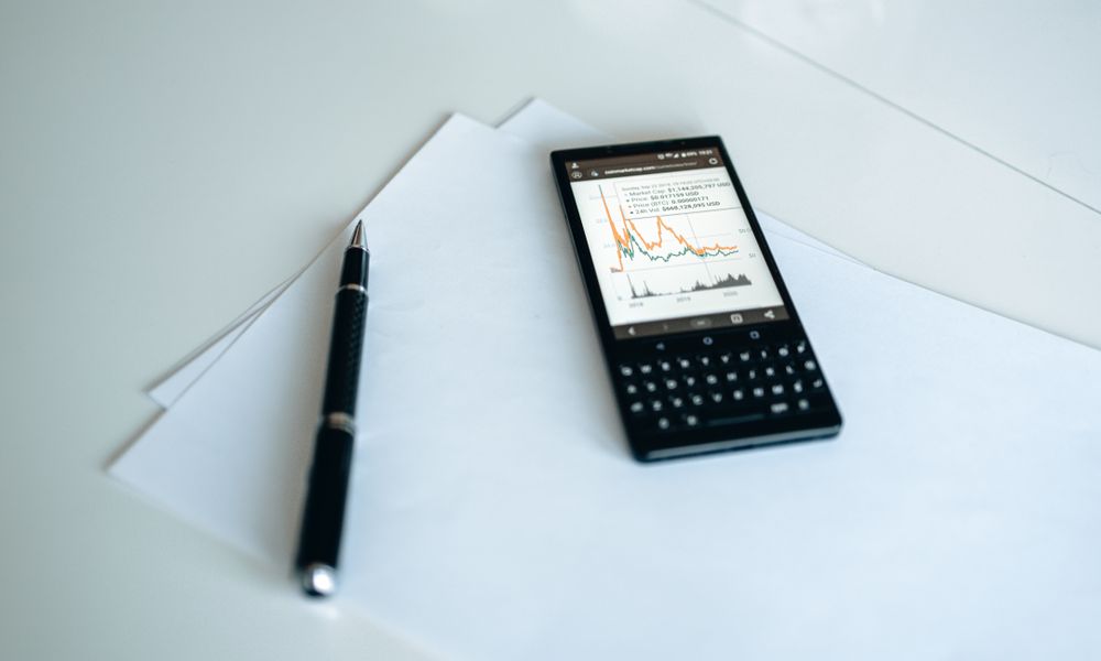 A smartphone displaying graphs placed on white paper with a pen on a table.