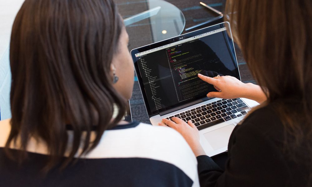 Two women working together on software programming indoors, focusing on code.