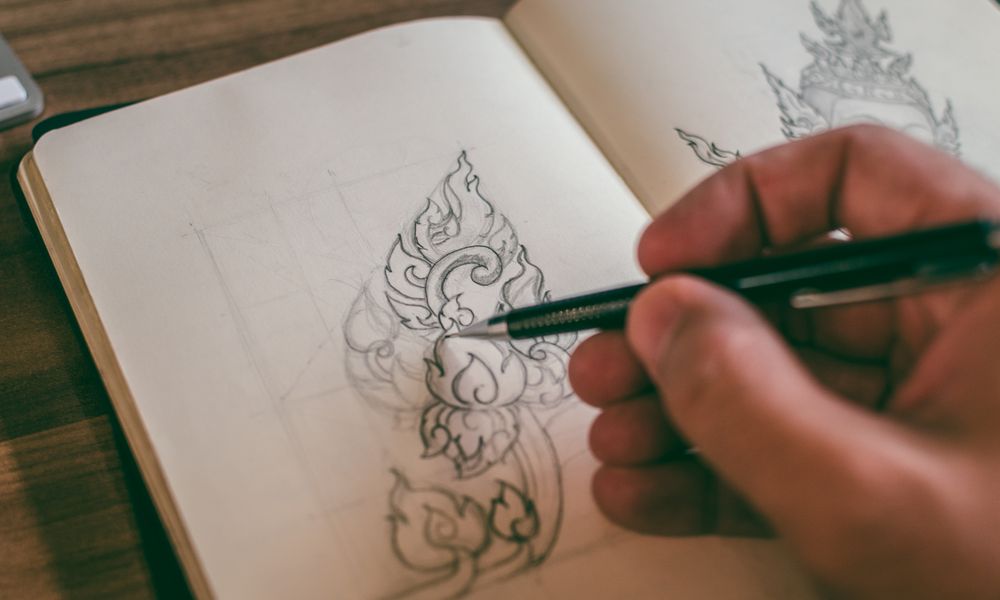 Close-up of a hand sketching detailed design in a sketchbook with mechanical pencil.