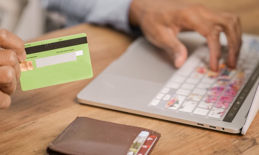 Person using a credit card for an online purchase on a laptop at a wooden table.
