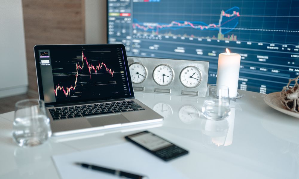 A modern workspace featuring financial charts and multiple clocks on a white table, ideal for trading.