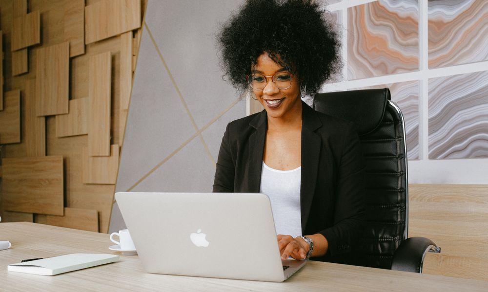 Smiling woman working remotely on a laptop in a stylish office setting.