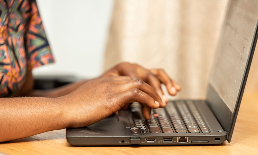 Detailed view of African hands typing on a laptop, shot indoors.