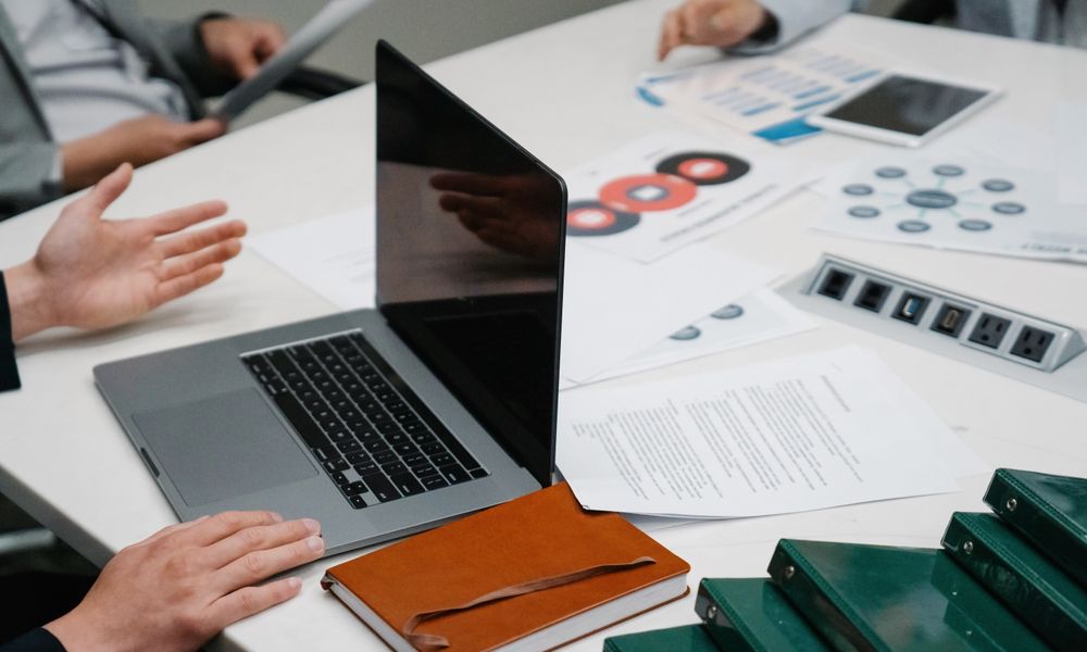 Close-up of a business meeting table with a laptop, documents, and discussion underway.