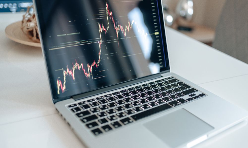 Laptop showing cryptocurrency market data on a white table, indoors.