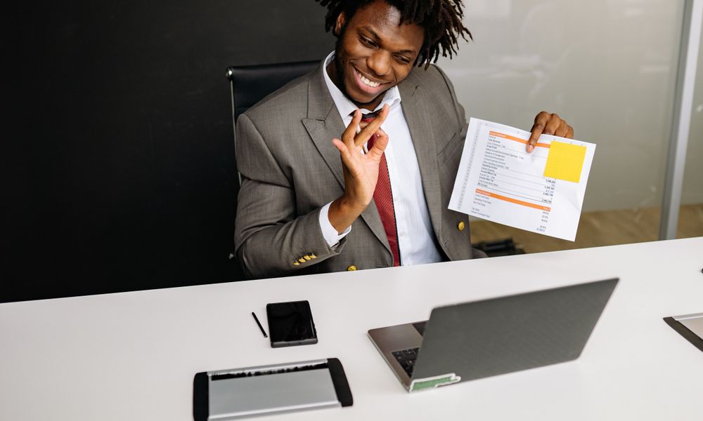 Smiling professional in a suit holds documents during a video call in an office setting.