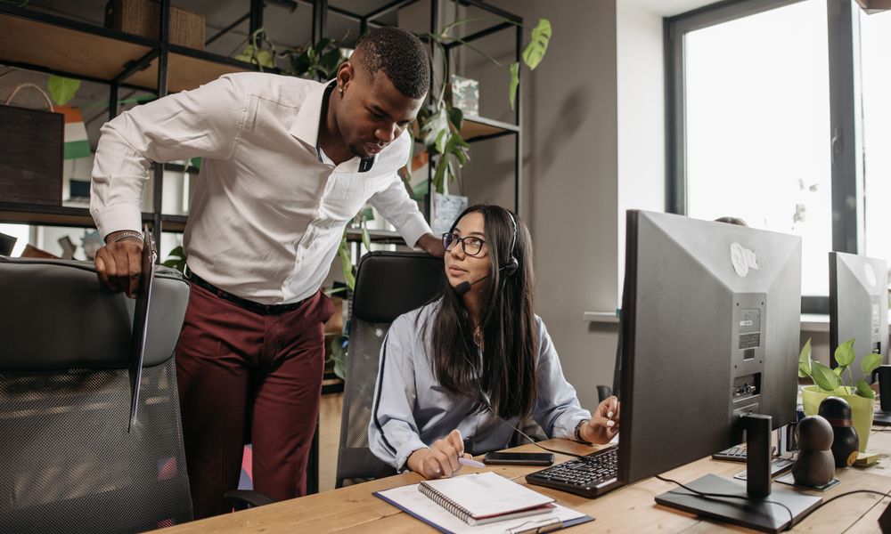 Two colleagues discuss projects at the office with computers and notebooks. Ideal for business and technology themes.