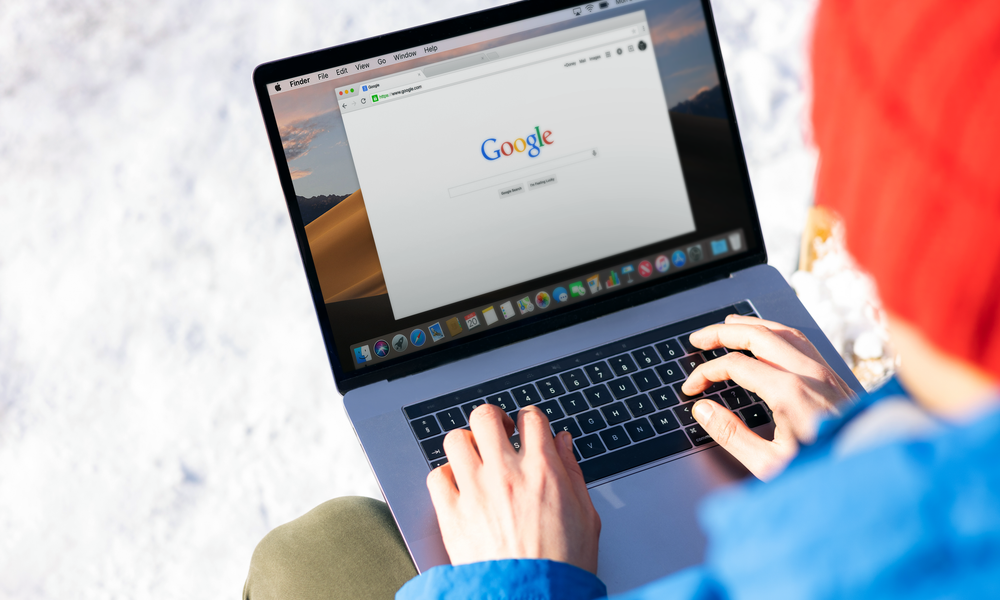 Individual typing on a laptop outdoors with snow, accessing the internet.