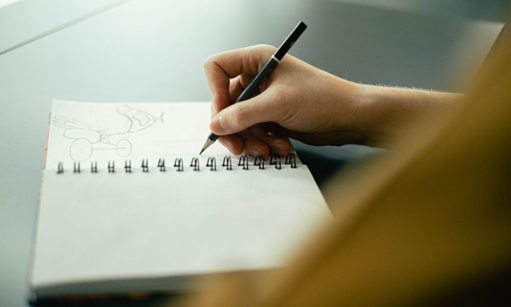 Hand sketching in a notebook with a pencil, focusing on creativity and planning.