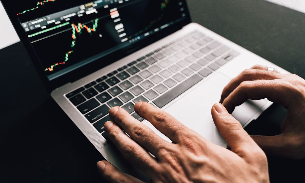 Close-up of hands typing on a laptop with stock market graphs, ideal for finance or business themes.
