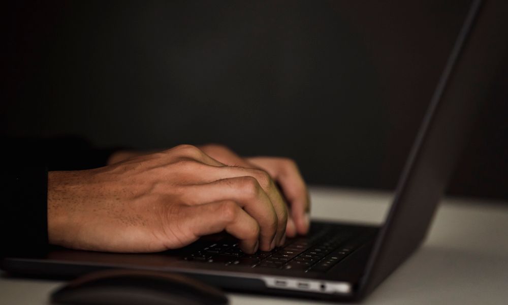 Crop unrecognizable person surfing internet on contemporary netbook and typing on keyboard in dark workspace