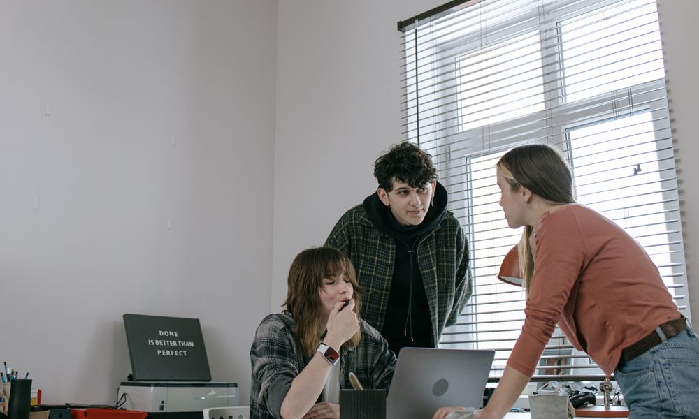 Team of young adults brainstorming ideas and discussing strategies around a laptop in a modern workplace.