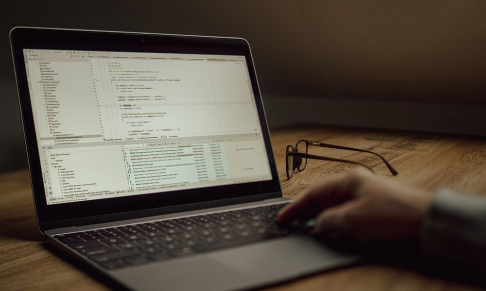 Person working on programming code on a laptop indoors. Glasses on the table.