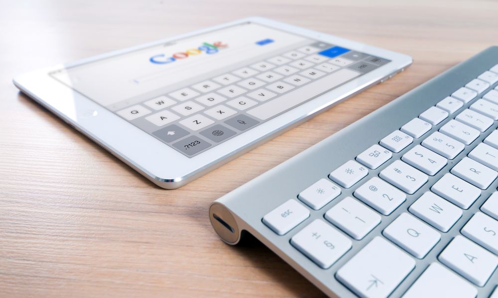 A modern tablet displaying a search engine logo next to a wireless keyboard on a wooden desk.