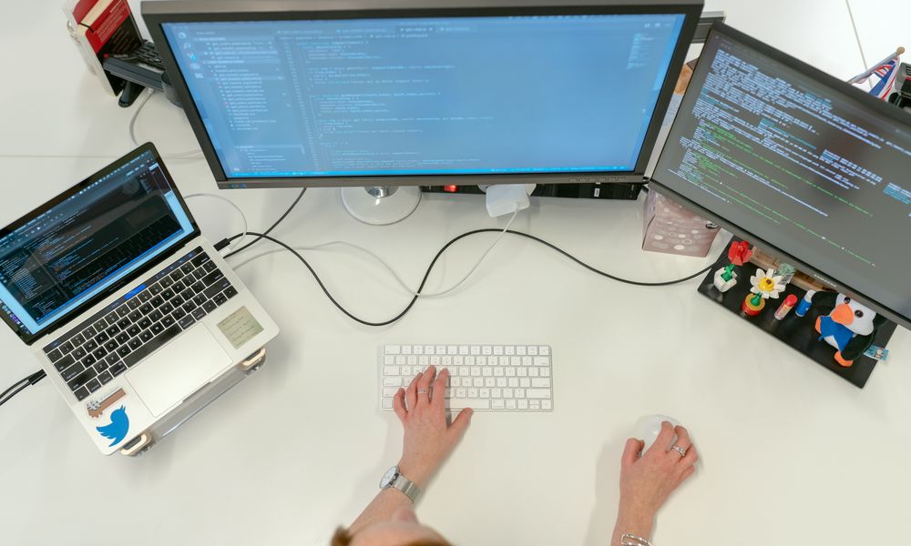 A female software engineer coding on dual monitors and a laptop in an office setting.