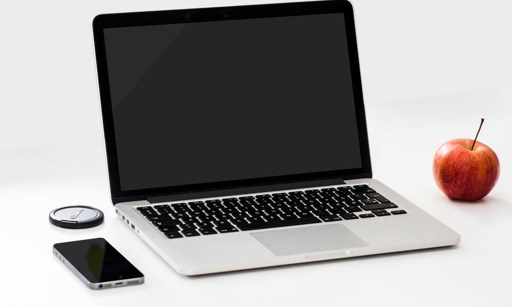 A minimalist workspace featuring a laptop, smartphone, and an apple on a clean white desk.
