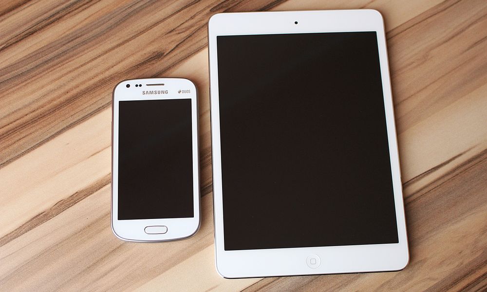 A white smartphone and tablet placed on a wooden table, showcasing technology contrast.