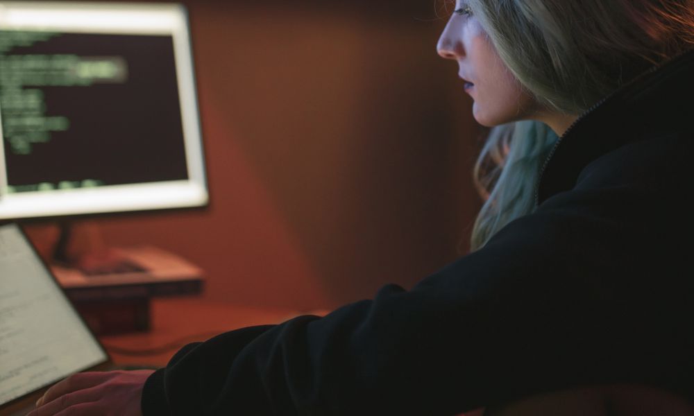 A woman working late on a laptop with code displayed on the screen in a dark room.