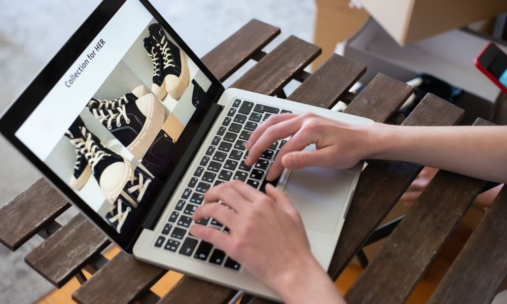 Hands of a person browsing a Collection for HER on an online shoe store using a laptop.