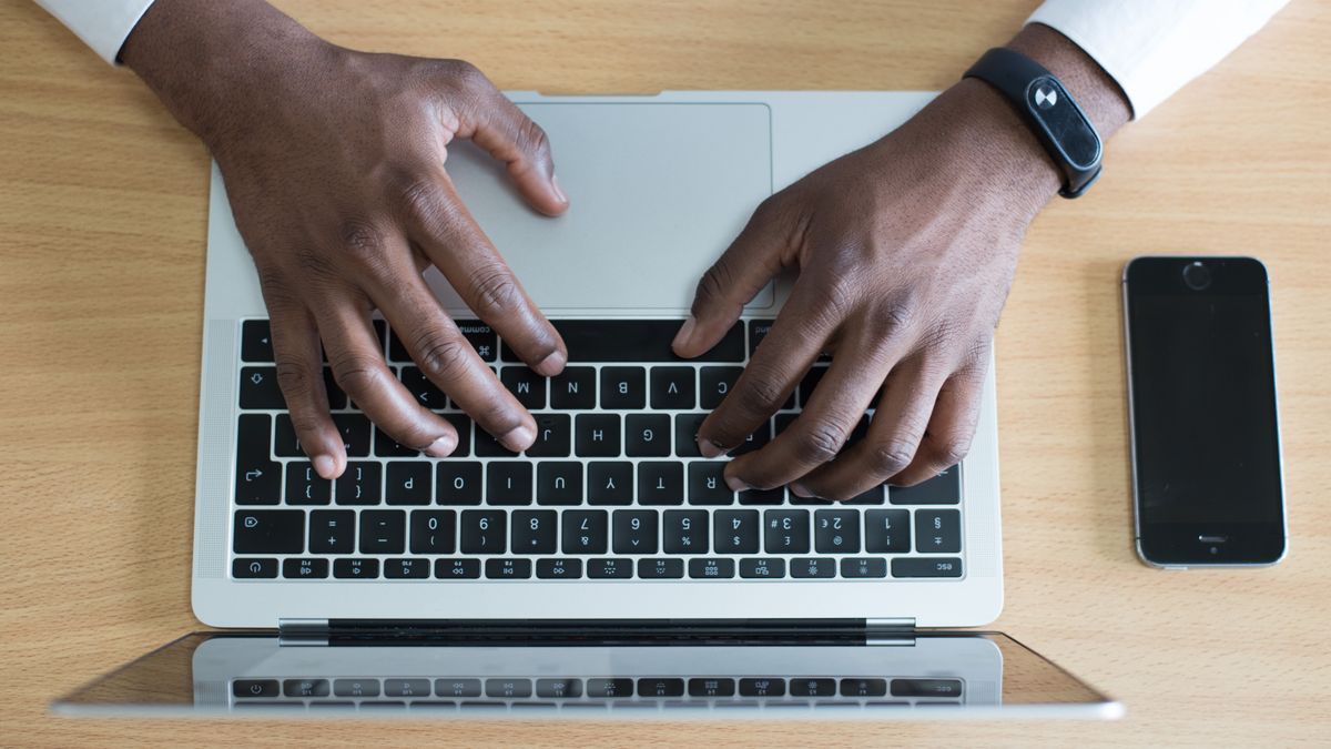 Person typing on a laptop with a smartphone nearby, showcasing modern technology use.