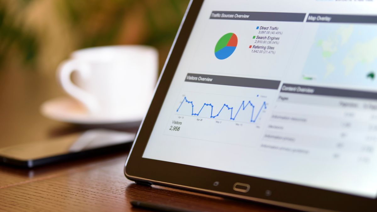 Close-up of a tablet displaying analytics charts on a wooden office desk, alongside a smartphone and coffee cup.