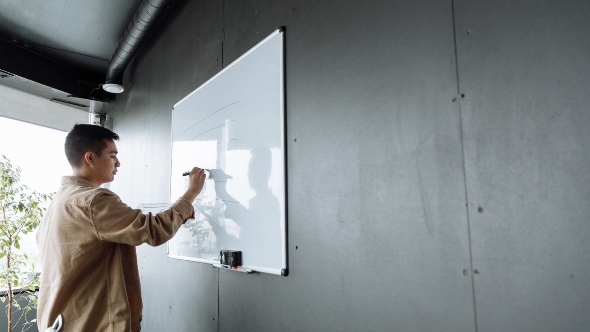 Adult writing on a whiteboard in modern office setting.