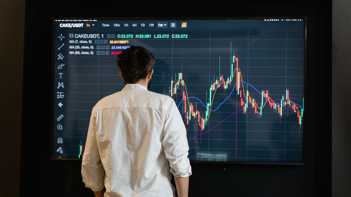 Back view of a trader analyzing cryptocurrency data on a monitor indoors.