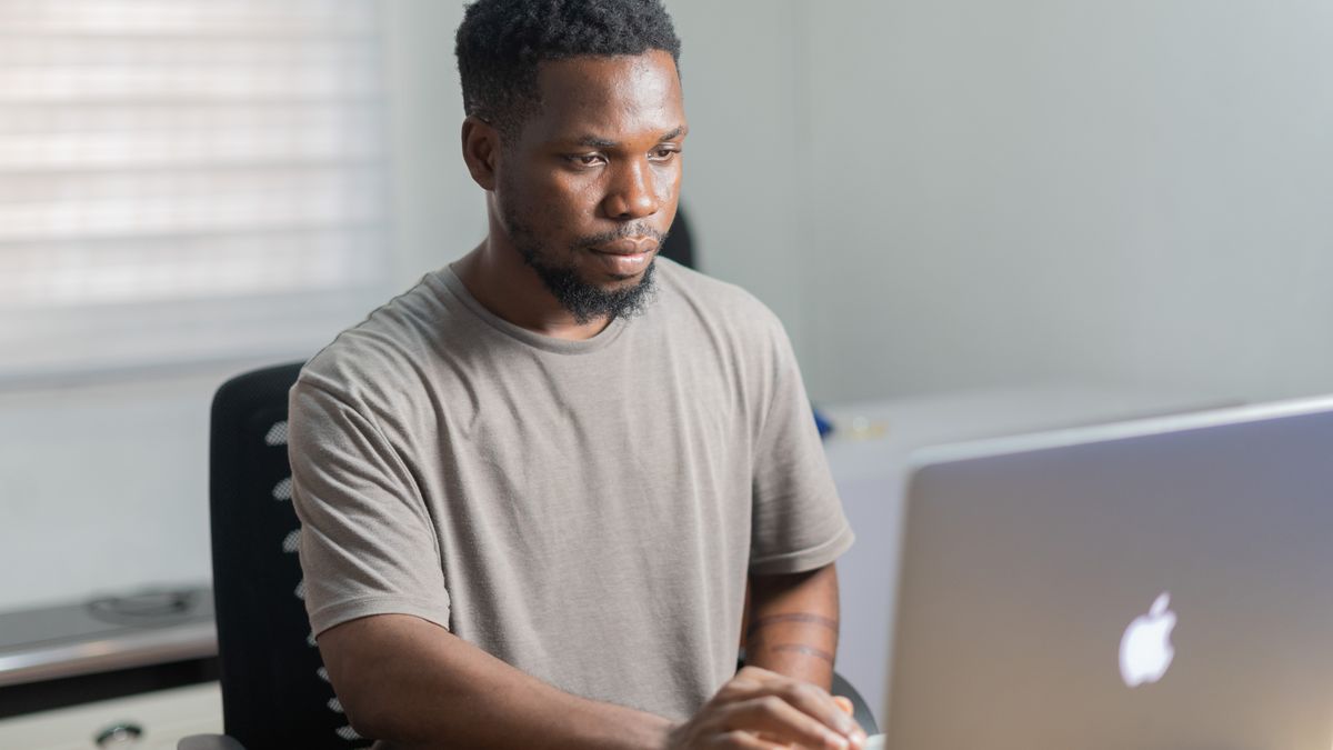 African American man working remotely on a laptop in a well-lit indoor setting.
