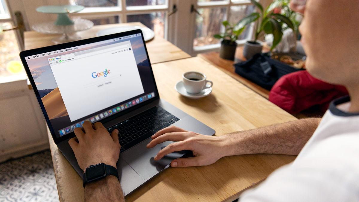 A person uses a laptop for internet browsing. A bright indoor setting with coffee on a wooden table.