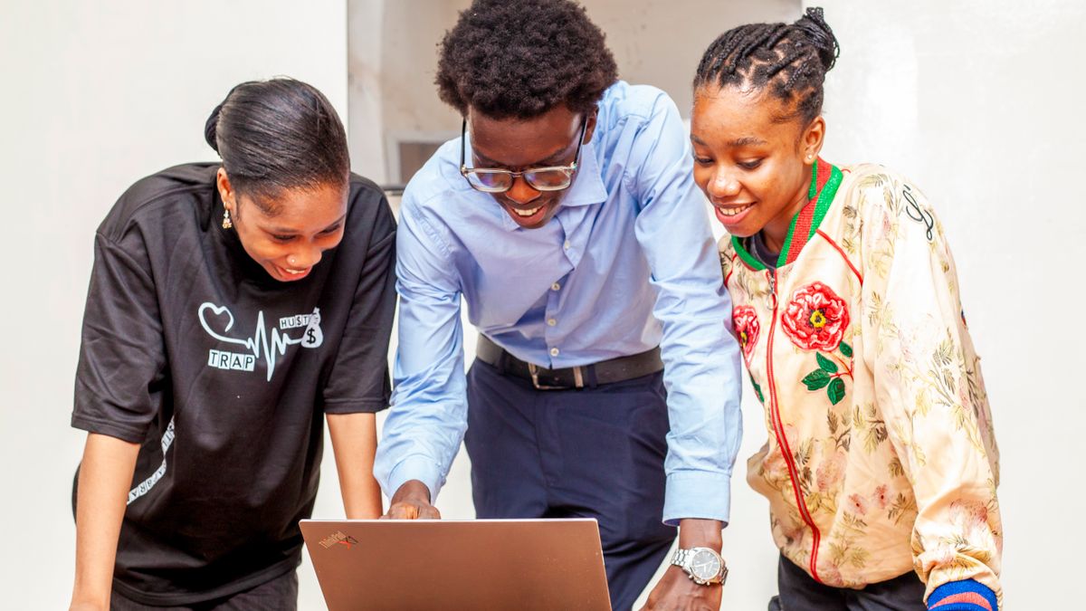 Three young adults collaborating on a laptop for a digital project indoors.