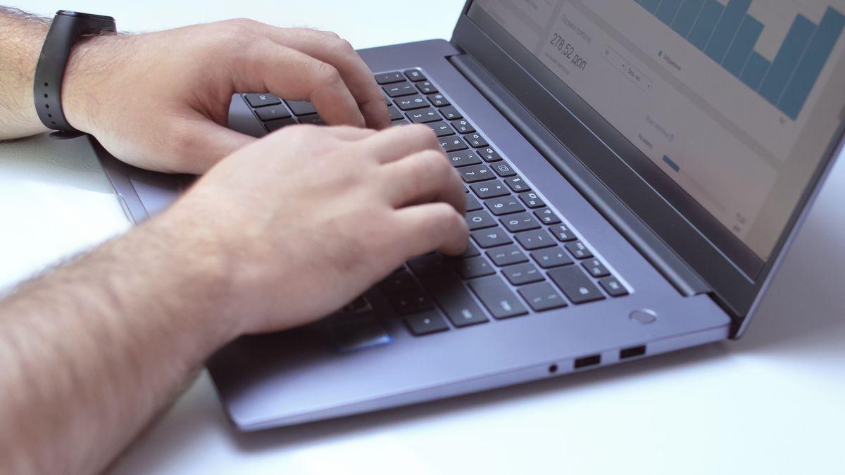 From above side view of crop unrecognizable male marketer working on netbook while using analytical software in office
