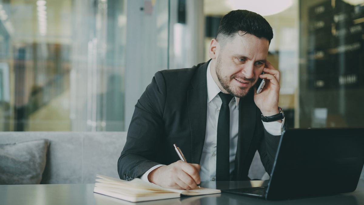 Professional man in suit multitasking with phone and laptop in modern office.
