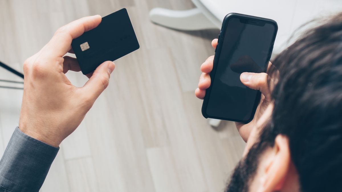 Close-up of man holding a smartphone and credit card, making an online payment indoors.
