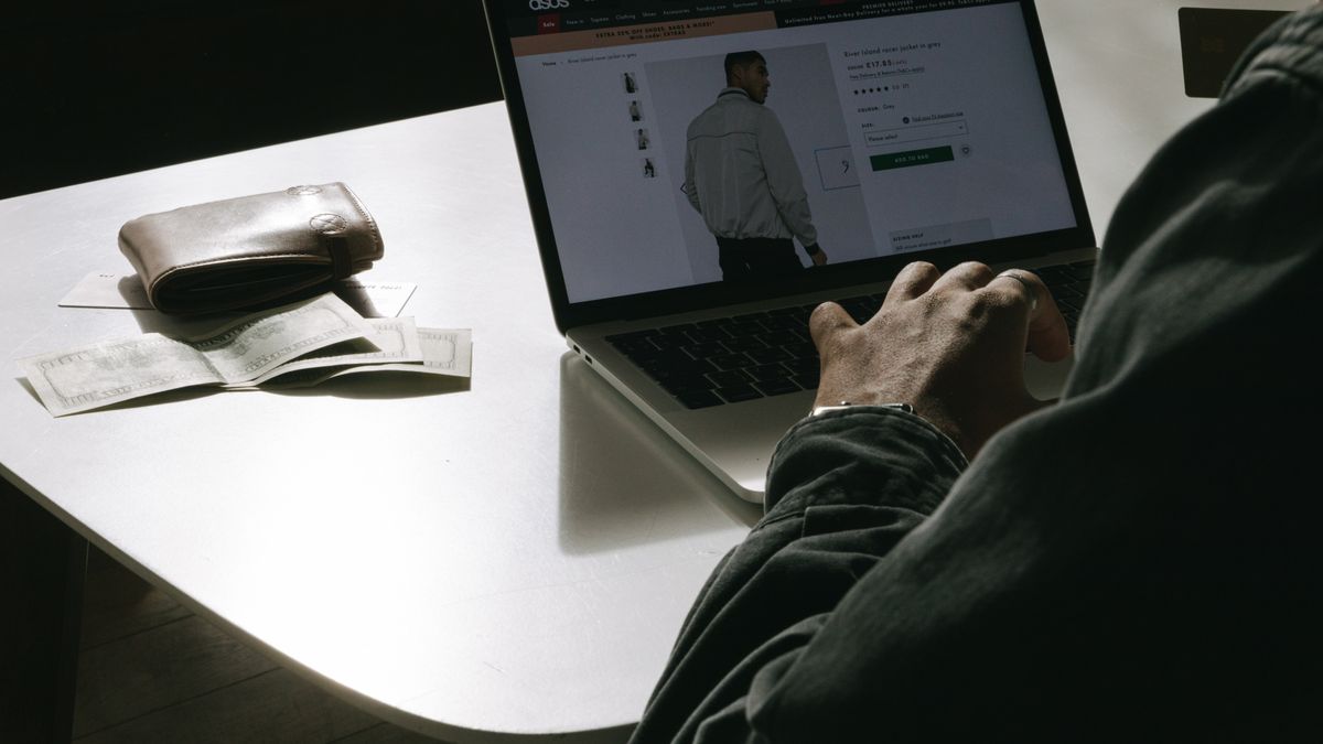 Adult man shopping for clothes online at home using a laptop, with a wallet on the table.