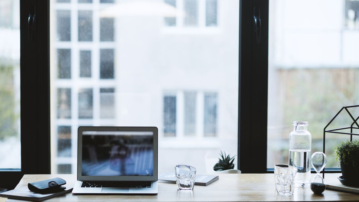 Sleek office desk setup featuring a laptop, glass of water, and open window view.