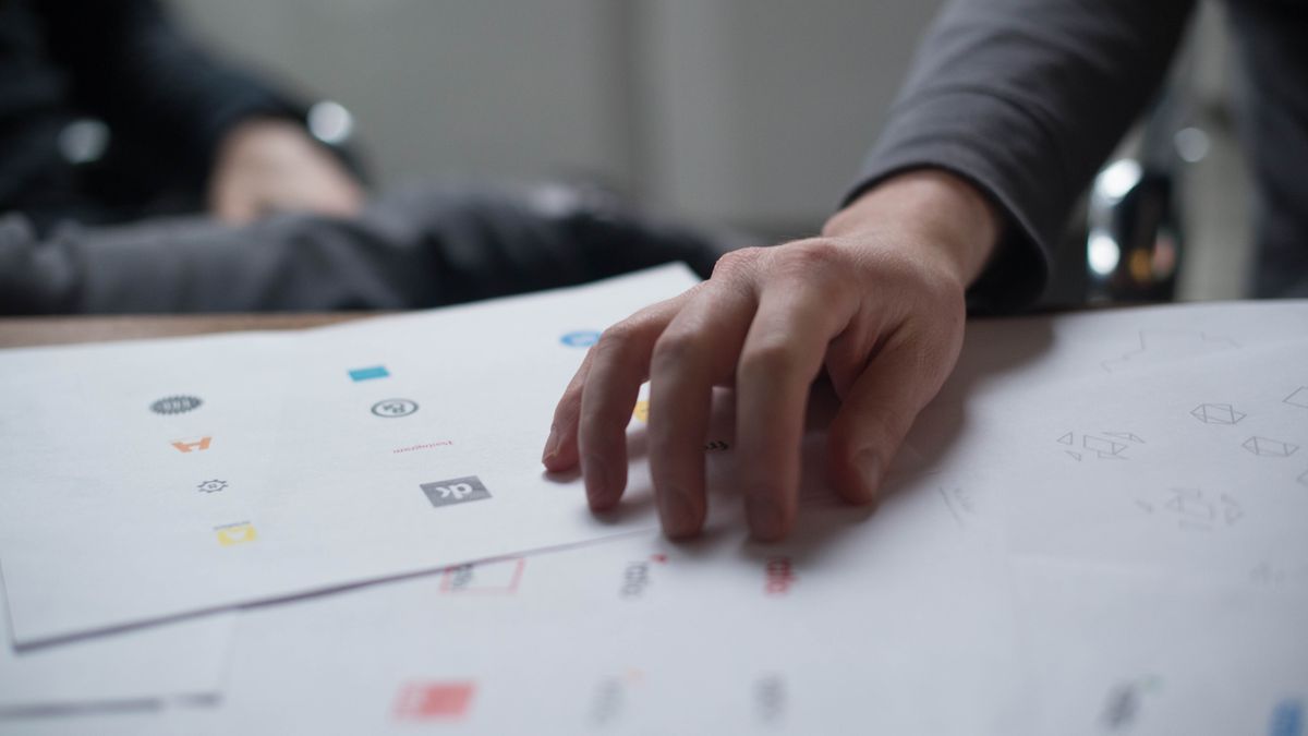 A close-up shot of a hand reviewing various logo designs on paper, ideal for business concepts.
